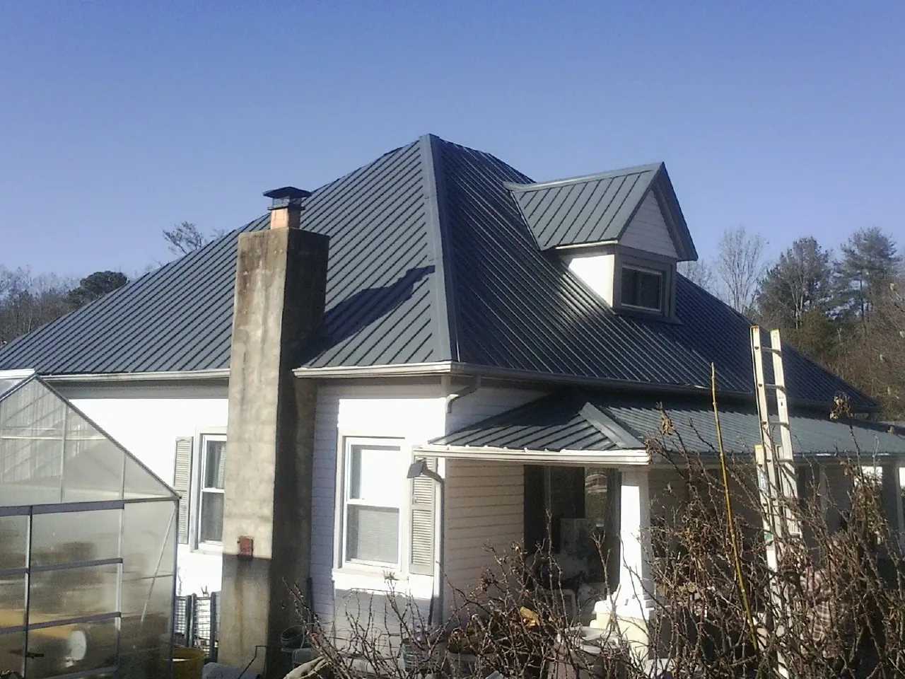 Dark blue standing seam metal roof on a white farmhouse with dormer — Slate & Tile Roof Repair by Roofing Brothers in Belgrade