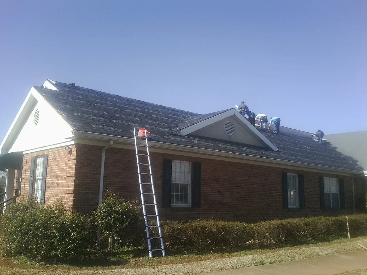 Crew tearing shingles off a brick ranch roof with a ladder set — Emergency Roof Repair work by our crew in Belgrade